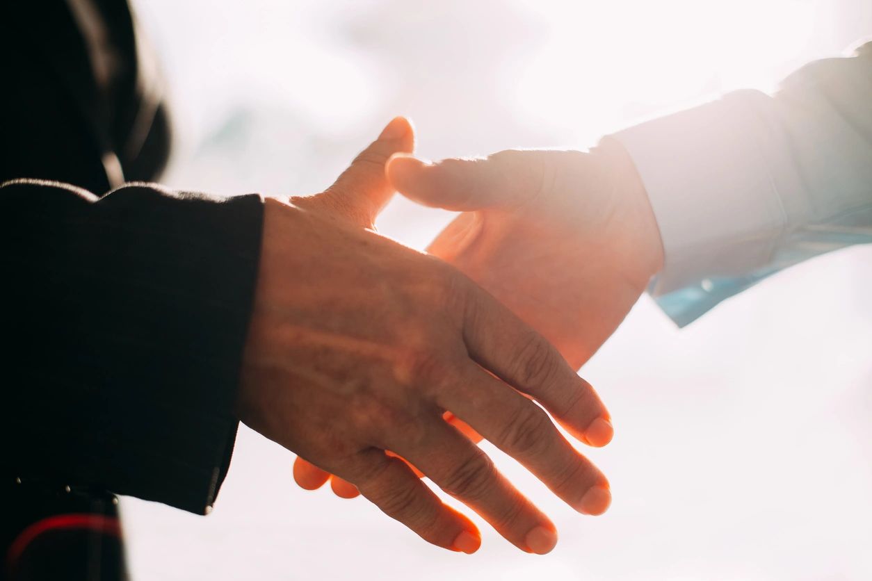 Two people shaking hands in front of a sky background