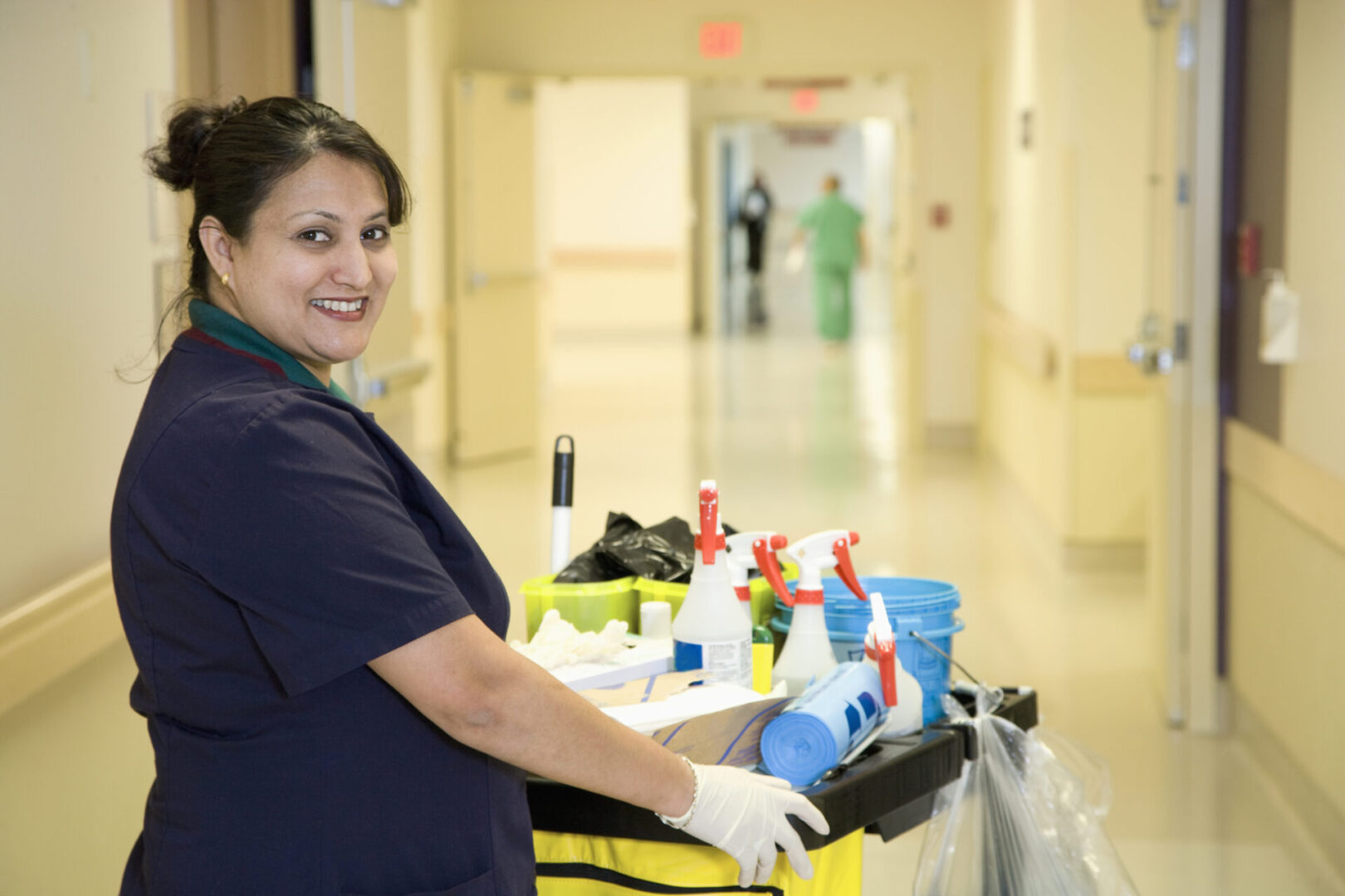 A woman in blue shirt holding cleaning supplies.