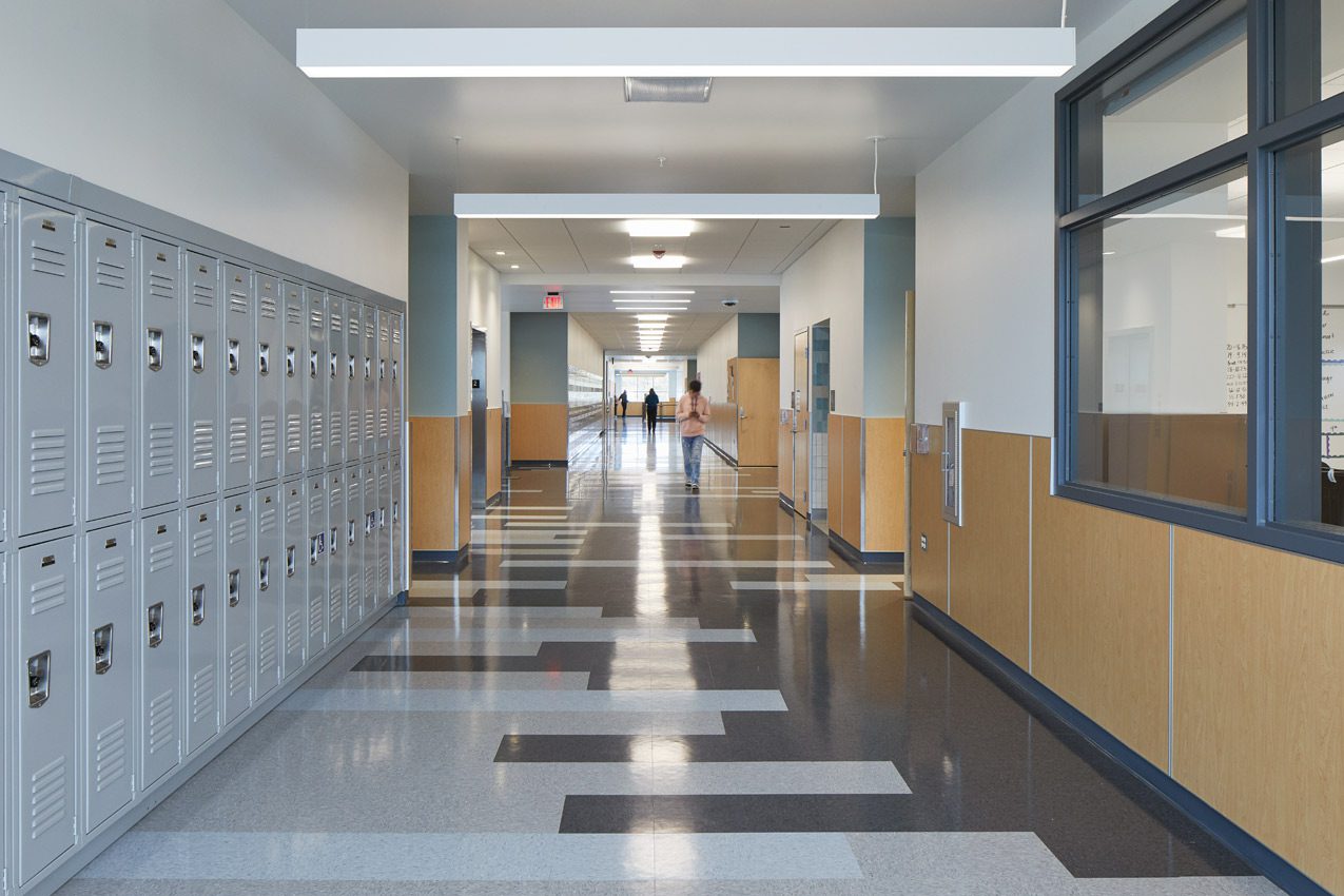 A hallway with many lockers and two people walking.